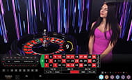 Live Dealer sits behind a roulette table as part of the Mansion Casino live gaming suite.